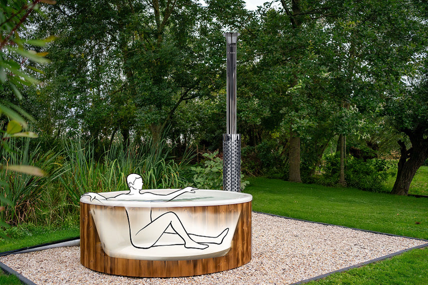 Outdoor view of a wood fired hot tub with integrated stove pipe surrounded by trees and greenery on gravel base