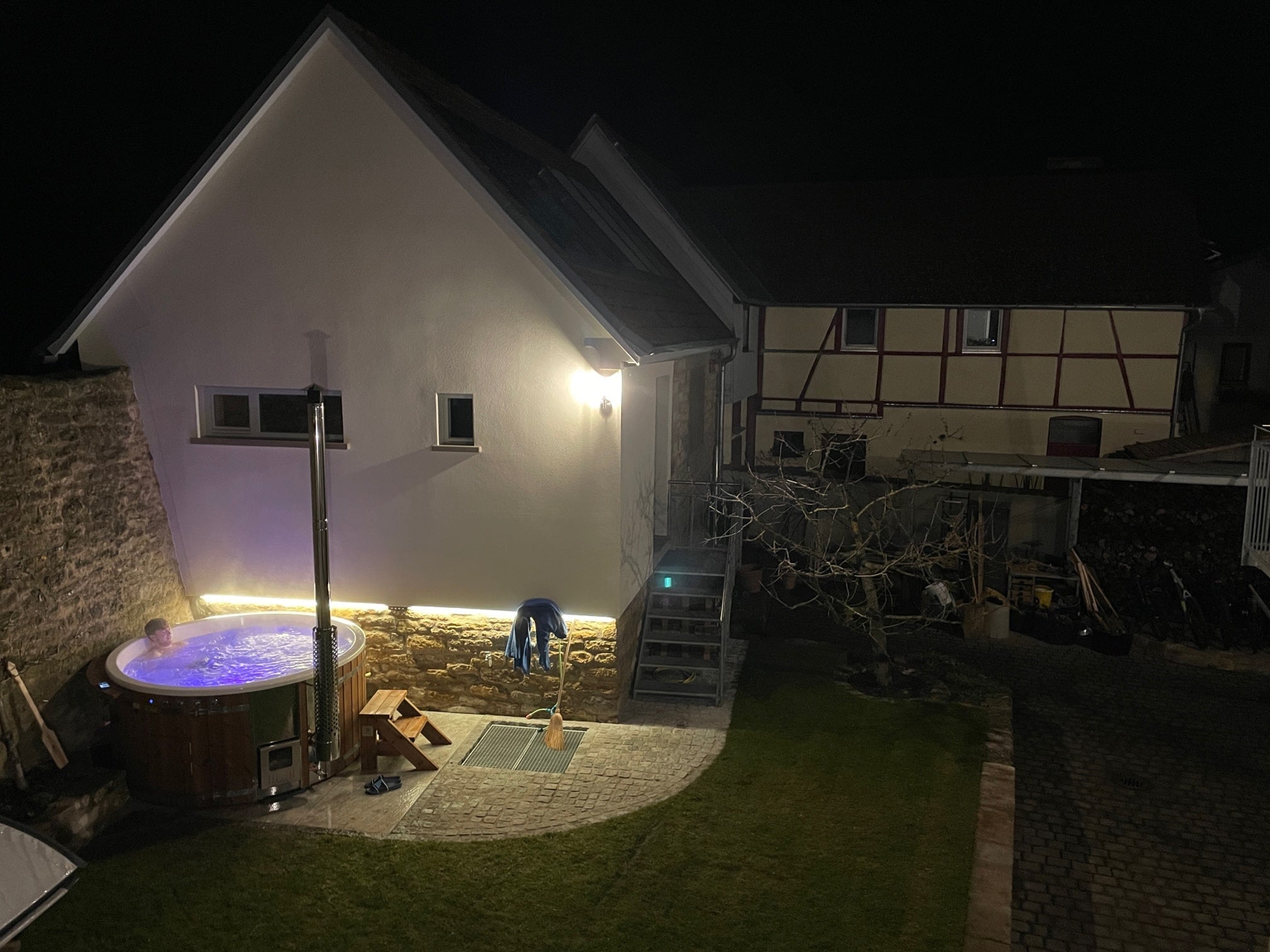 Gardenvity wood fired hot tub beside country house at night with warm outdoor lighting.