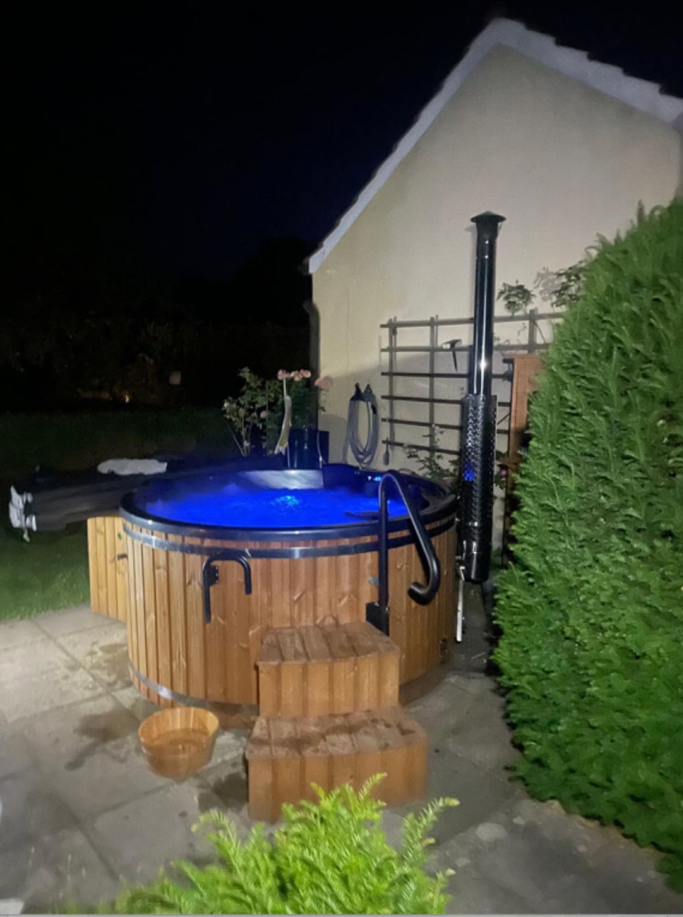 Gardenvity wood fired hot tub in backyard illuminated with blue LED lights at night