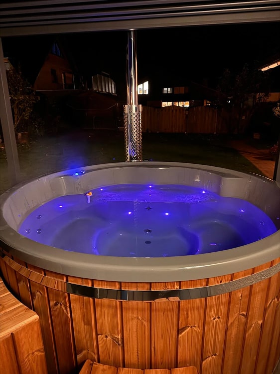 Gardenvity wood fired hot tub surrounded by fairy lights on wooden deck at night.